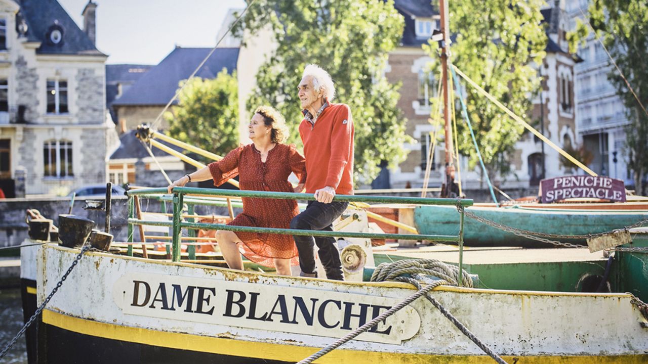 Une femme et un homme sur le devant d'une péniche qui regarde à l'horizon