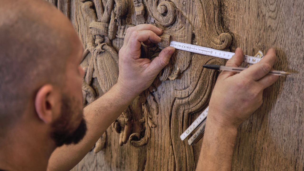 Un menuisier mesure une scupture pour la restaurer