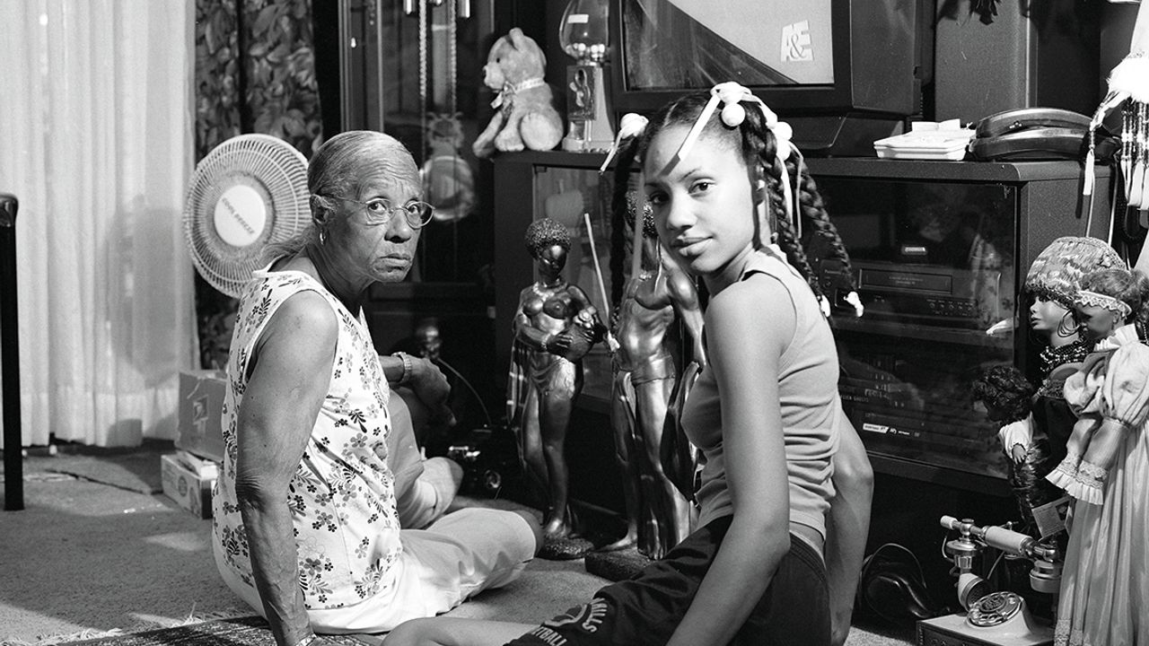 une grand mère et sa petite fille posent assises au sol dans un salon. photo en noir et blanc