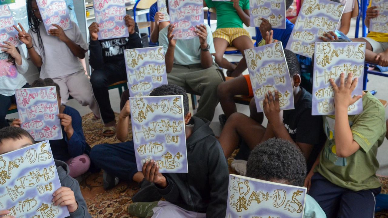 Des enfants dans une classe posent ensemble avec leurs fanzines qui couvrent leur tête. 