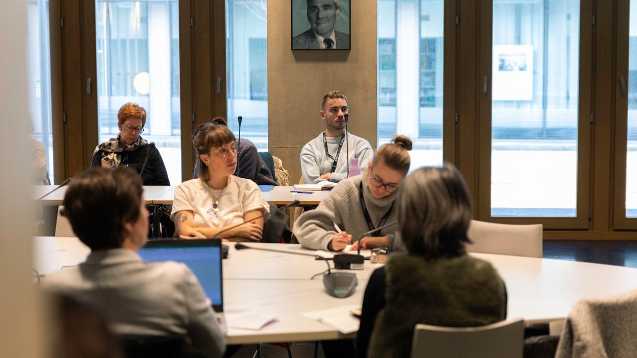 Des personnes autour d'une table en train d'écouter une présentation