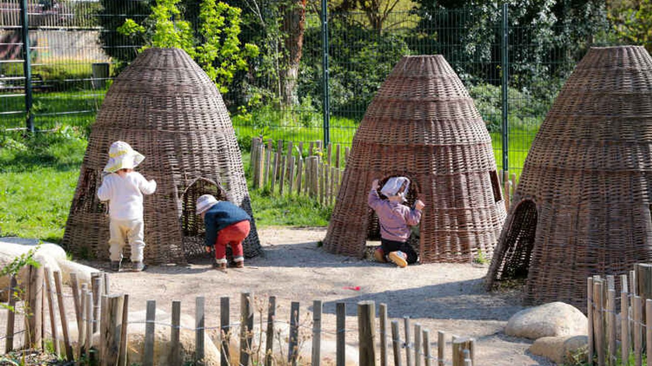 Des enfants explorent des cabanes en bois dans un espace vert?