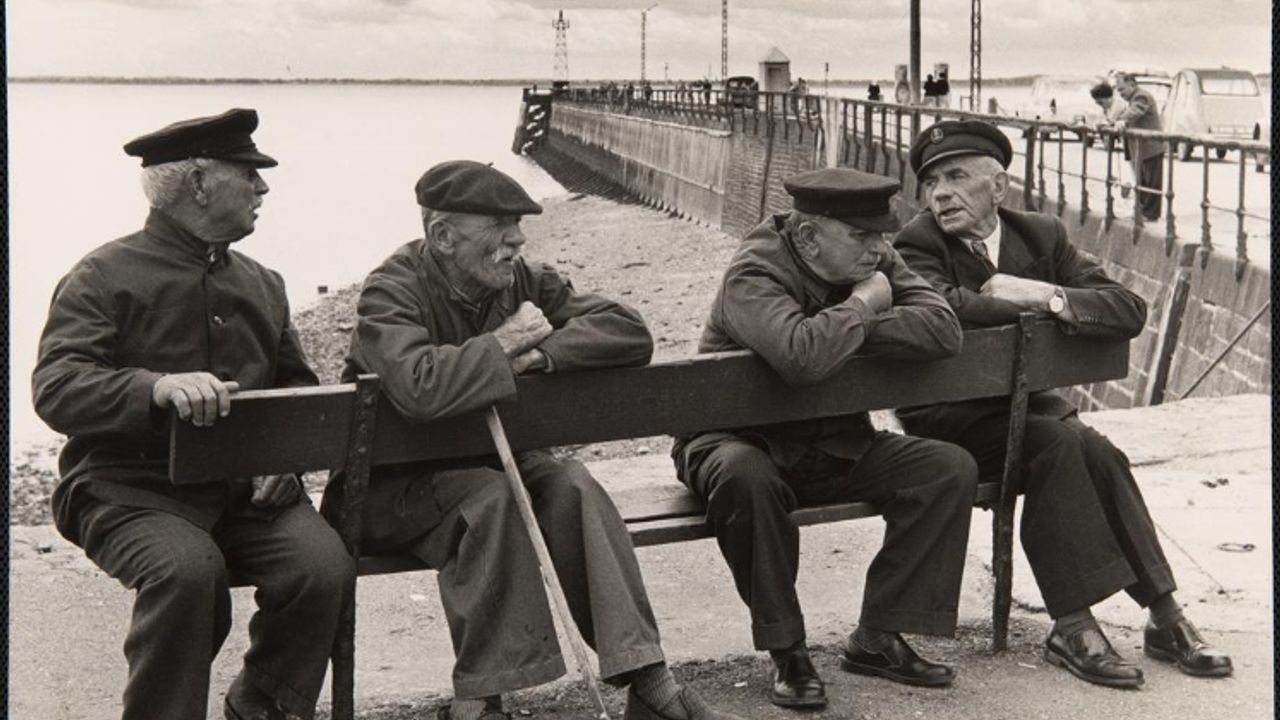 Des hommes portant des casquettes, assis sur un banc, au bord de la mer