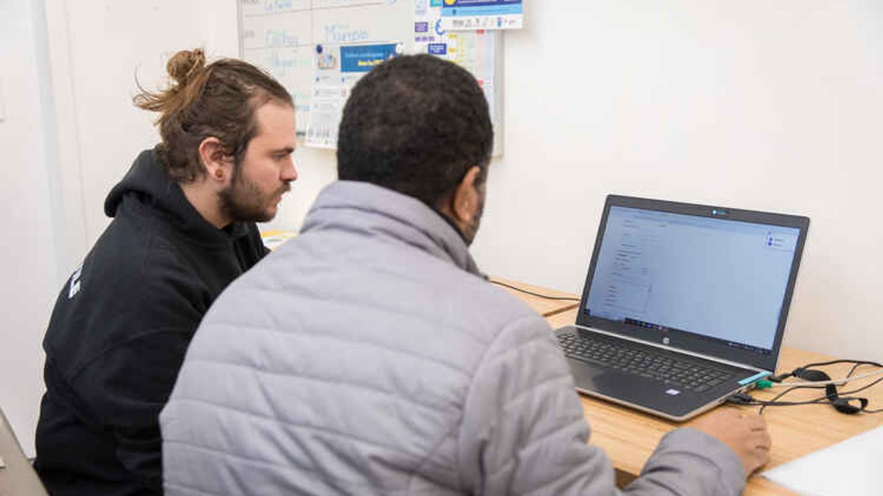 Une personne en aide une autre à réaliser des formalités en ligne
