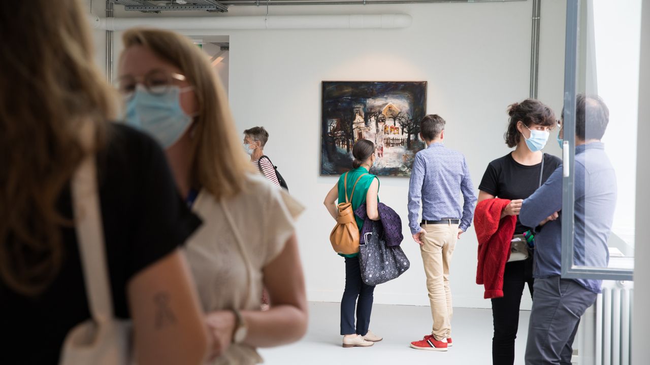 Des visiteurs regardent des oeuvres exposées dans une pièce.