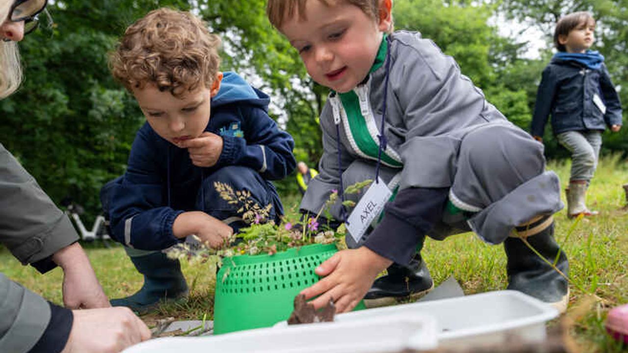 Deux enfants décorent une passoire avec des fleurs et herbes