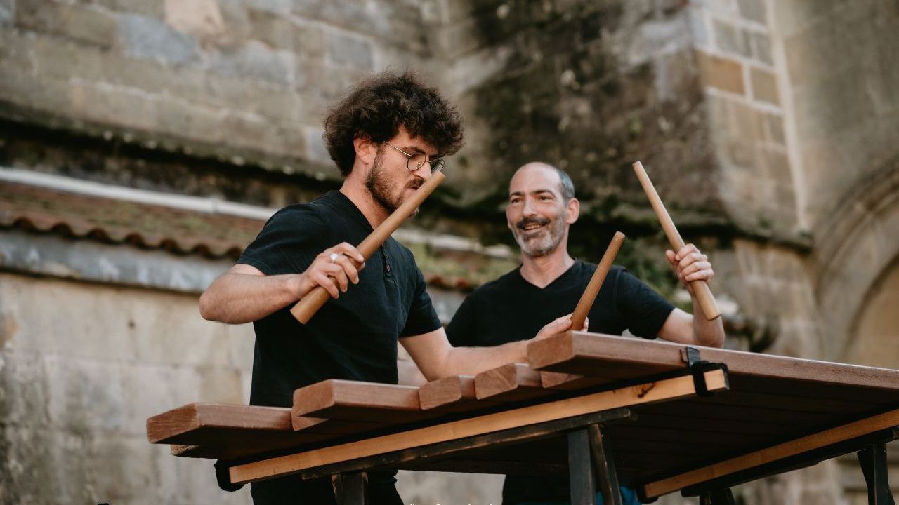 Deux musiciens frappent avec des batons sur une percussion traditionnelle basque faite de planches en bois