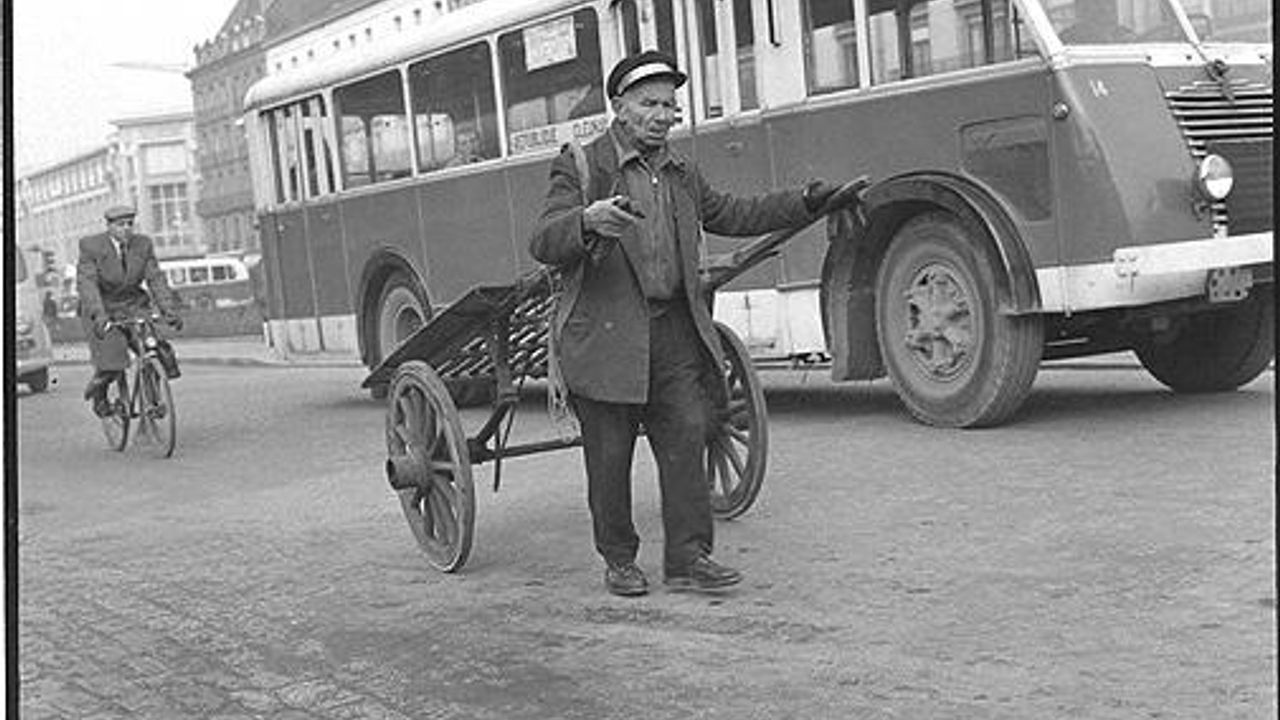 Photo d'un homme tirant une charrette, en arrière plan un bus et un homme sur un vélo.