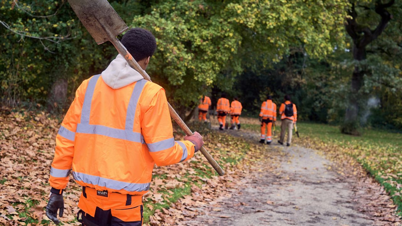 Des personnes vêtues d'un équipement de sécurité orange marchent, bêche en main, sur un sentier du parc de Bréquigny.