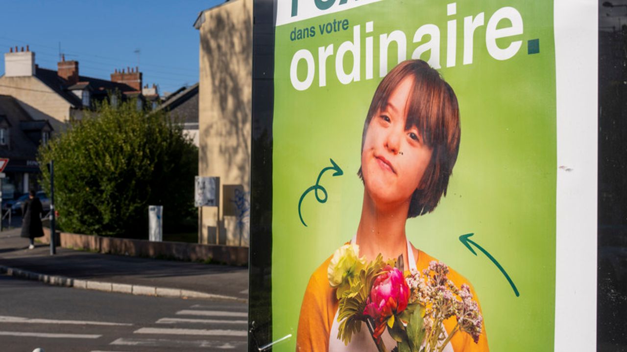 Dans la rue un panneau d'affichage Embauchez de l'extra dans votre ordinaire montre une jeune femme porteuse de trisomie 21 en situation de fleuriste avec un bouquet à la main