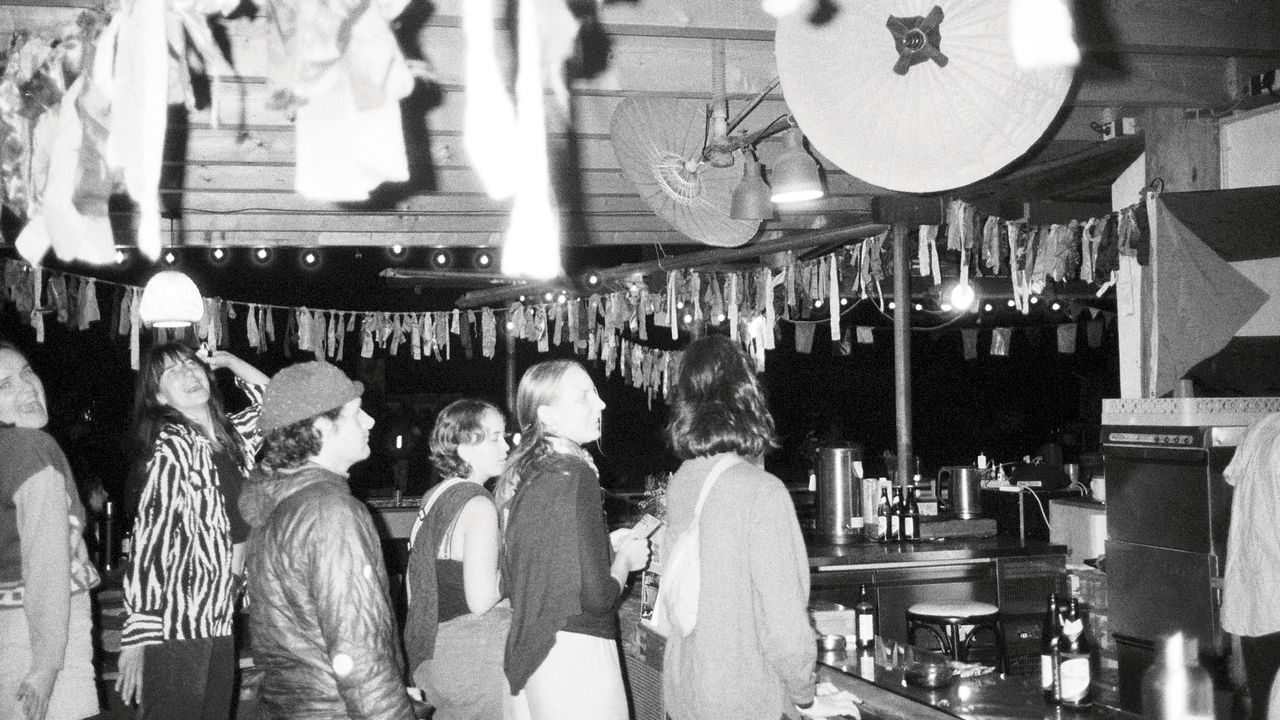 Black and white picture of people standing in line at the outside bar