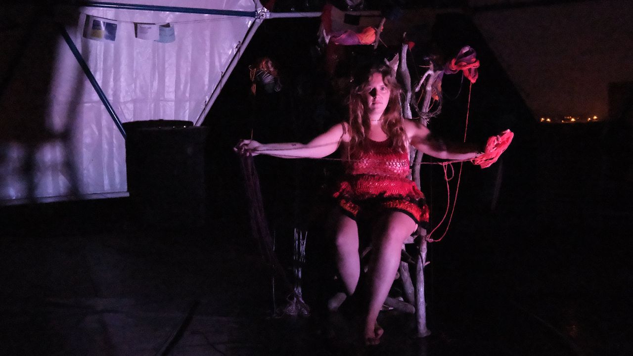 Person on a stage, sitting in a big chair decorated with yarn threads