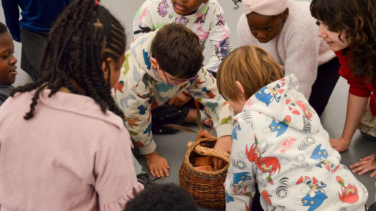 Des enfants regardent ce qui se trouve dans un panier en osier pendant la visite de l'exposition d'Hélène Bertin.