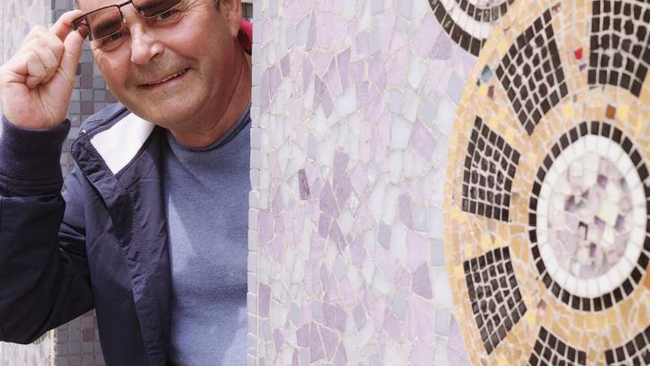 Daniel Enoch souriant et au premier plan des mosaïques qu'il aime tant