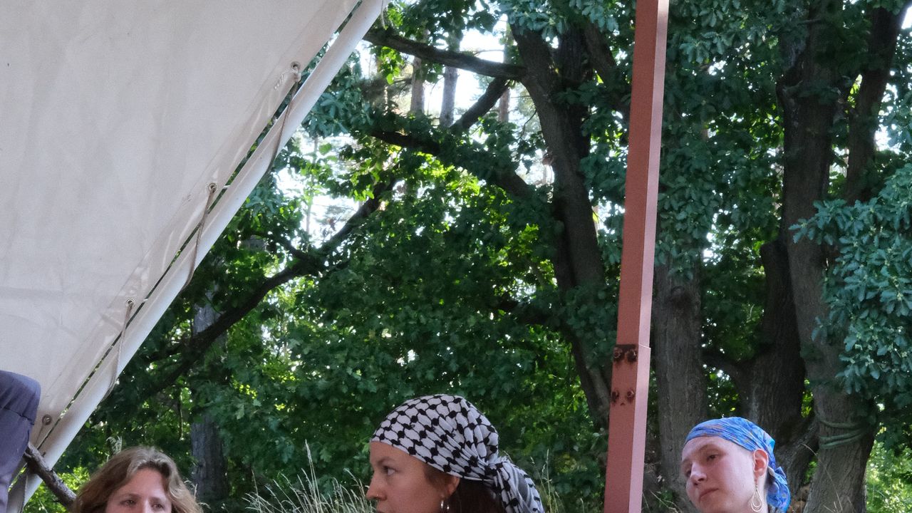 people sitting on the ground, one of them is talking at a microphone