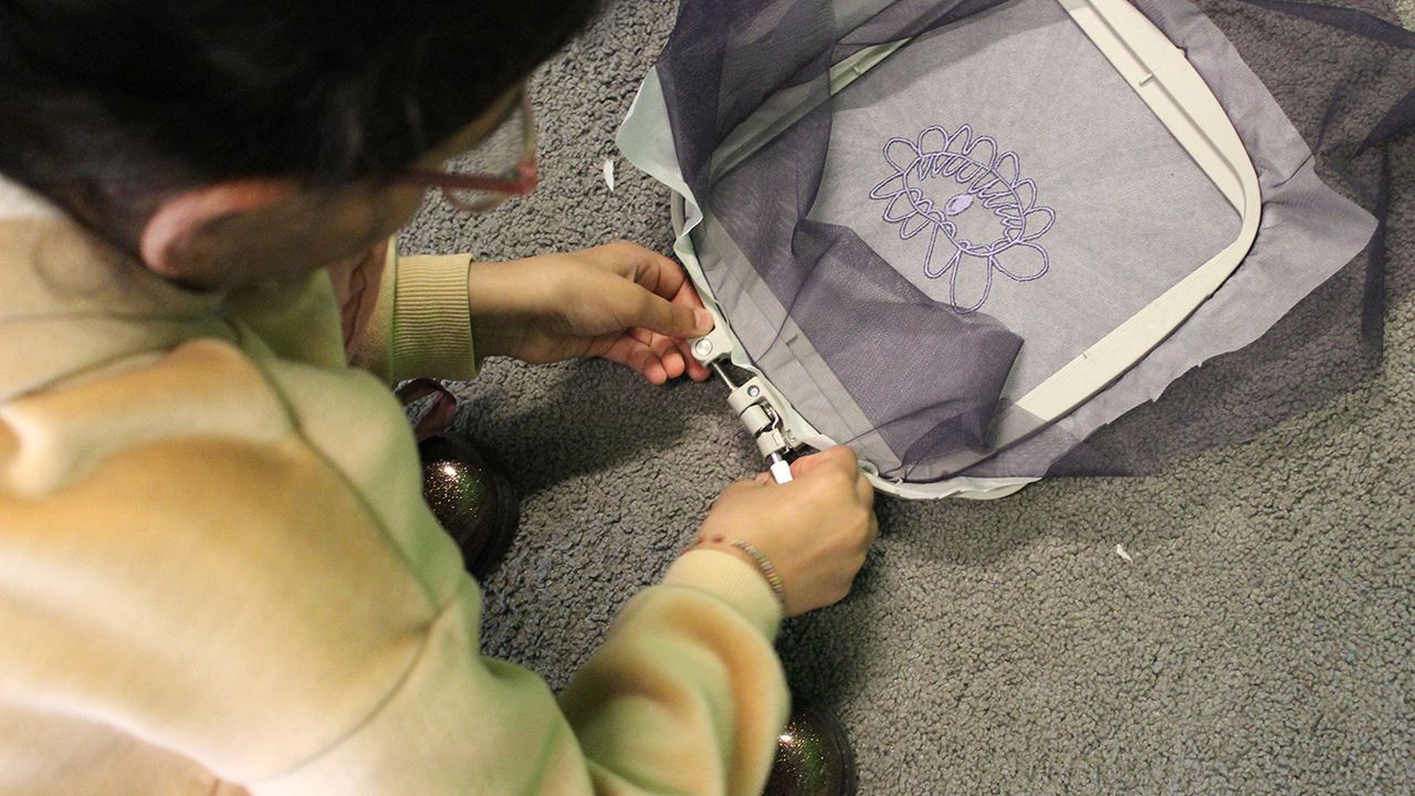 Une enfant enlève le cadre de son tissu violet brodé d'une fleur mauve.
