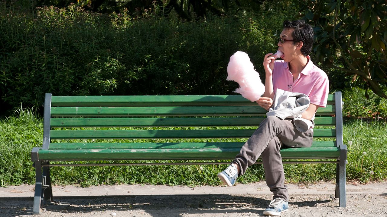 Banc public - Jeune homme vêtu de rose mangeant une barbe à papa rose