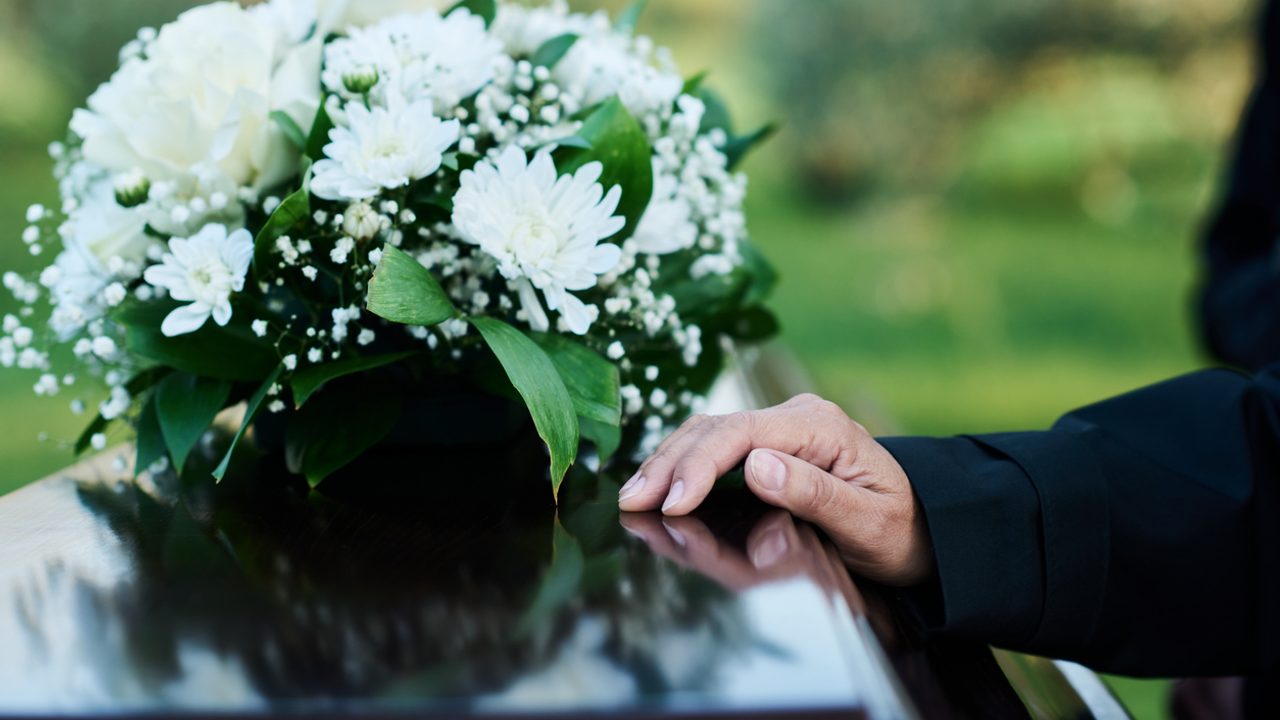 Une main sur un cercueil avec un bouquet de fleurs.