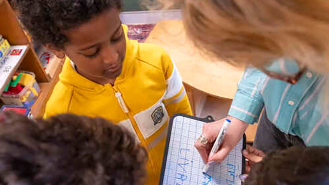 Des enfants et une enseignante écrivent le même mot en plusieurs langues sur une ardoise. 