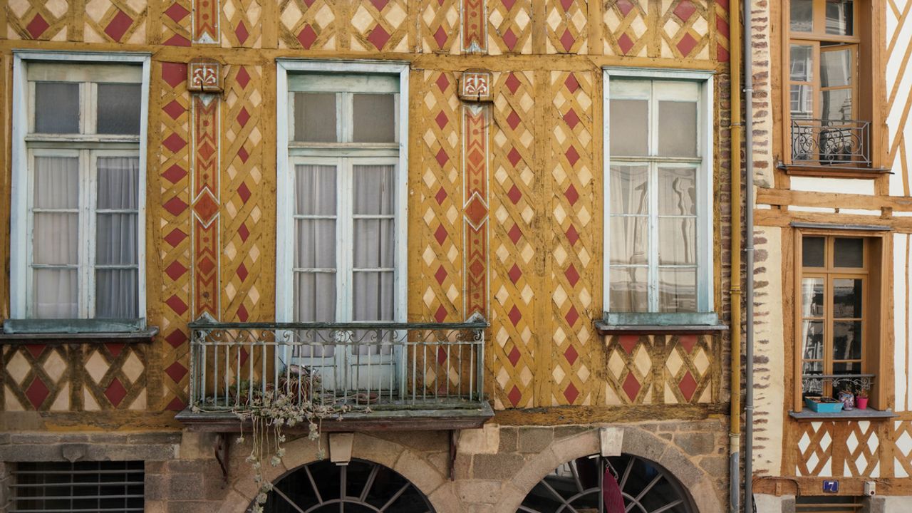 Vue sur une maison à pans de bois colorée dans la rue du chapitre : jaune, rouge et bleu animent la façade.