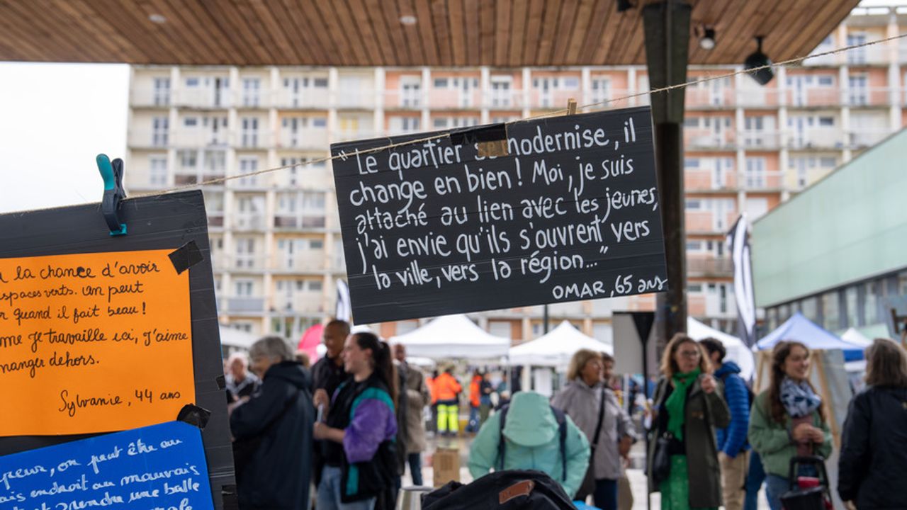 des pancartes avec des textes d'habitants sont accrochées dehors sous un préau. En arrière plan un immeuble.