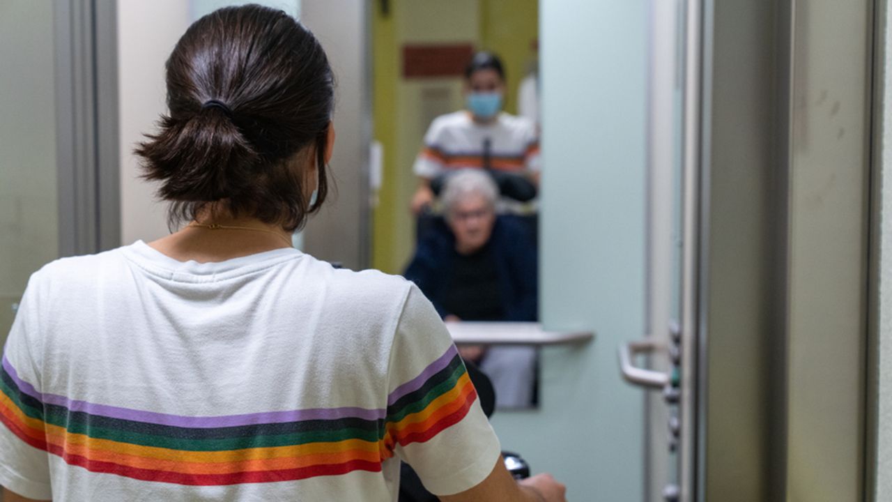 Jeune femme guidant une personne âgée en fauteuil roulant vers un ascenseur