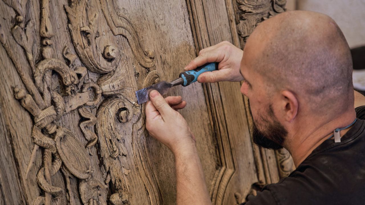 Un menuisier restaure les délicates sculptures de la porte de l'Hotel de ville avec un ciseau à bois.