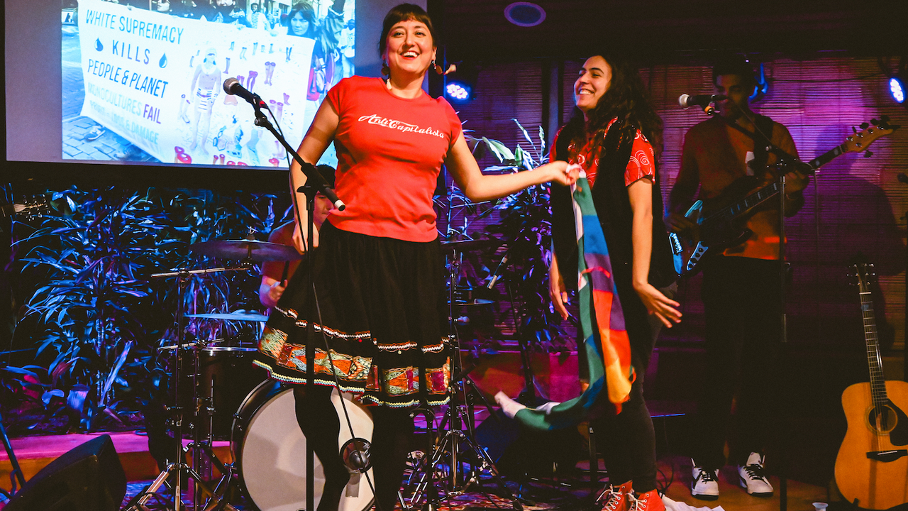 Two people standing on a stage indoors, surrounded by instruments.