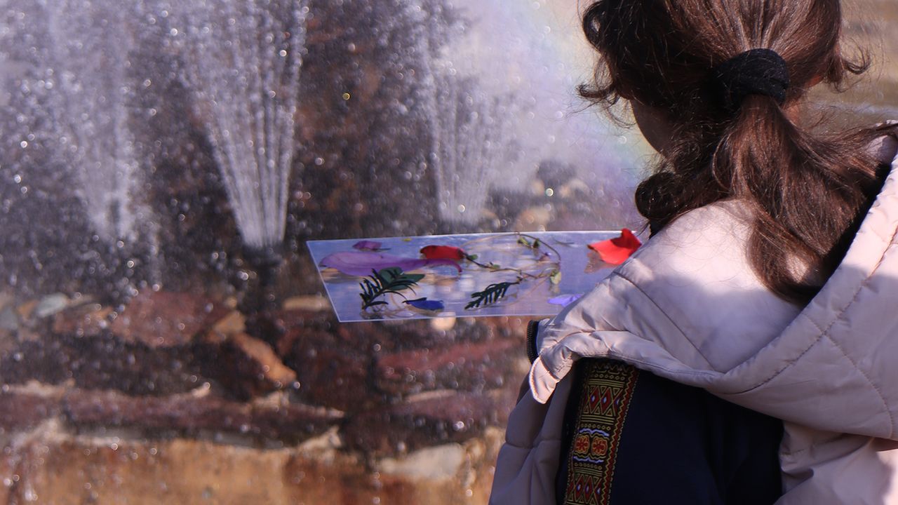 Une élève observe le jeu de reflets de la fontaine, sa composition en main.