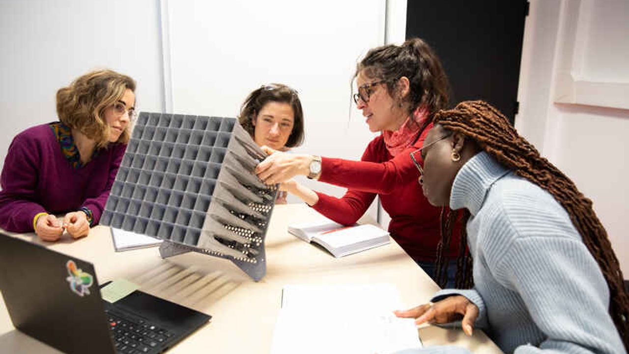 Quatre femmes assises autour d’une table sur laquelle est posée une maquette cubique. La deuxième femme en partant de la droite est la chercheuse de l’Insa Rennes, Maria Garcia Vigueras. Elle décrit le dessous de la maquette cubique aux trois autres femmes attentives.
