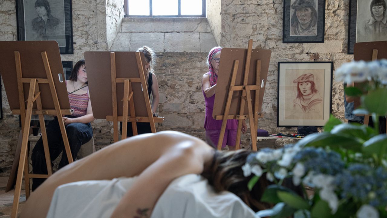 Le dos d'une femme nue en premier plan, et en second plan des personnes dessinant sur des chevalets